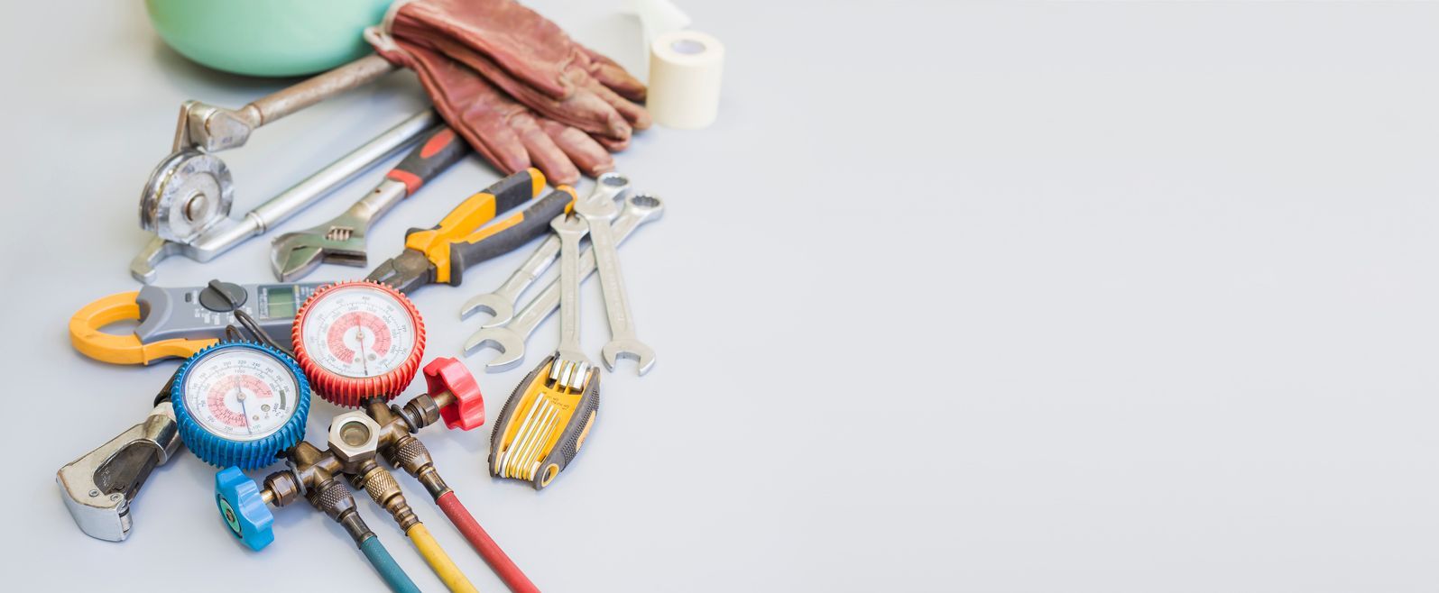 A set of HVAC tools, including gauges, wrenches, and pliers, on a gray surface.