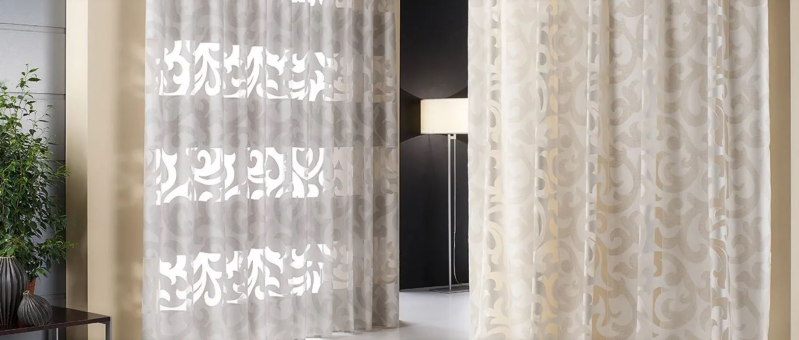 Tende trasparenti con motivi decorativi incorniciano un televisore a parete in una stanza illuminata da una luce soffusa.