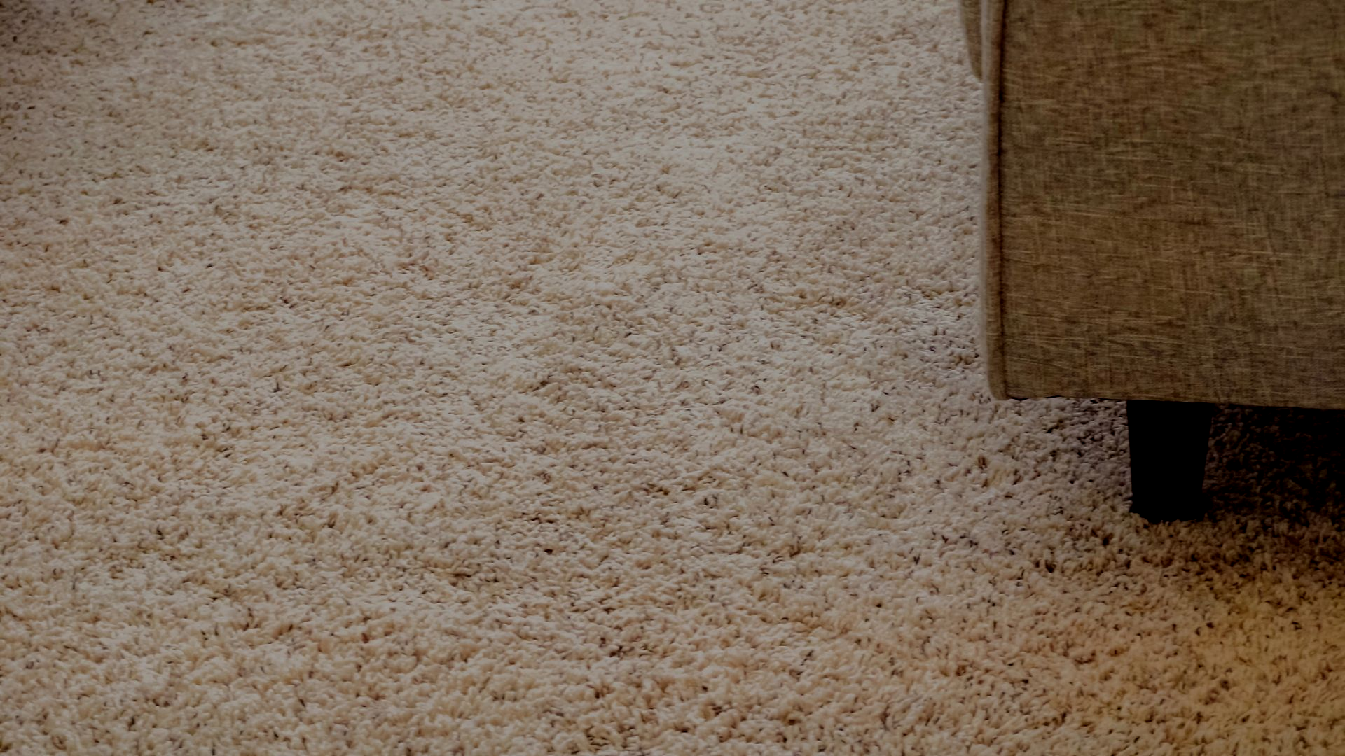 Primo piano di un tappeto beige accanto all'angolo di un divano marrone.