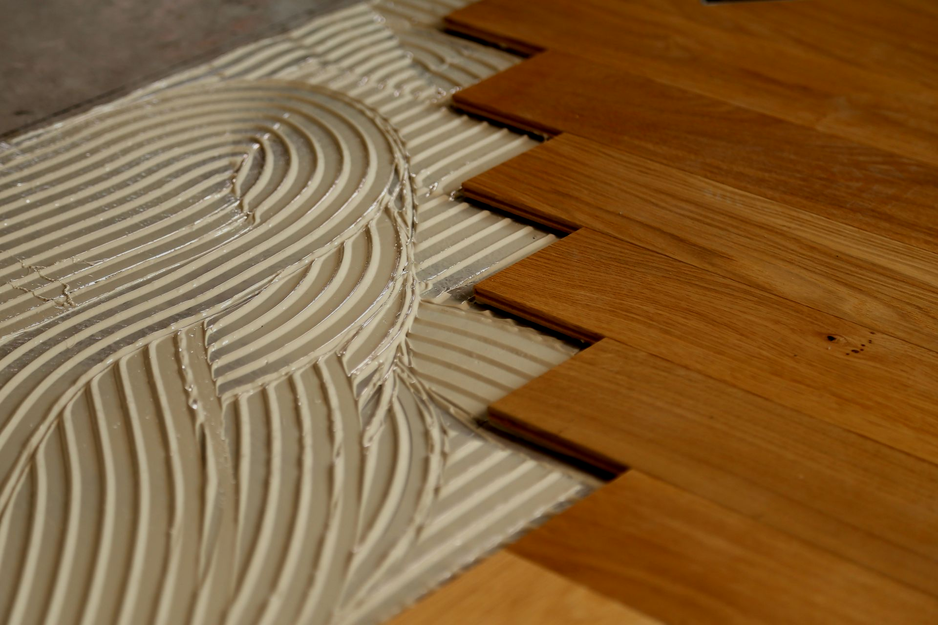 Primo piano di legno e adesivo bianco spalmato in scanalature a zig-zag su una superficie piastrellata.