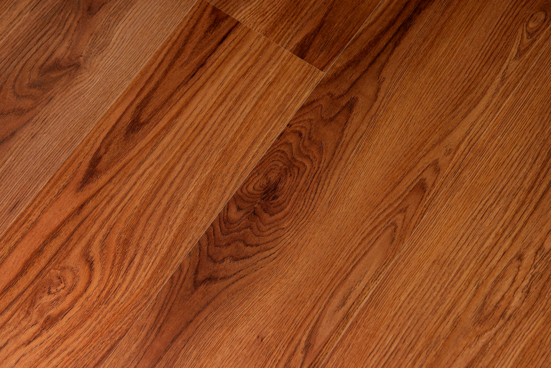 Primo piano di un pavimento in legno bruno-rossastro con venature ben visibili e assi disposte in diagonale.