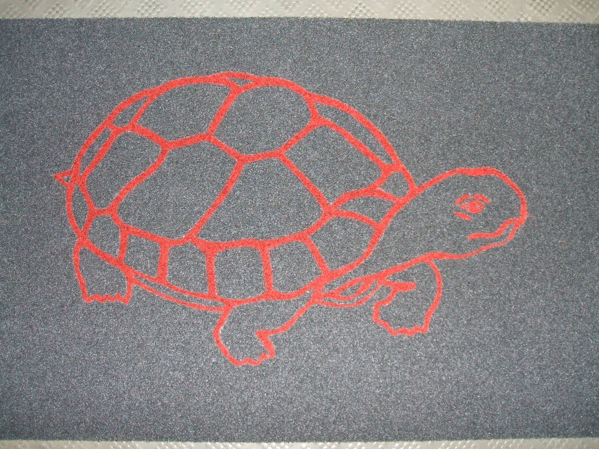 Disegno di una tartaruga realizzato con il gesso rosso su un pavimento o asfalto scuro.