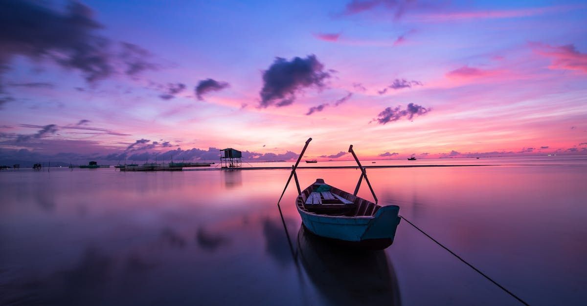 Boat at sunset, reflecting on calm water; pink and purple sky.