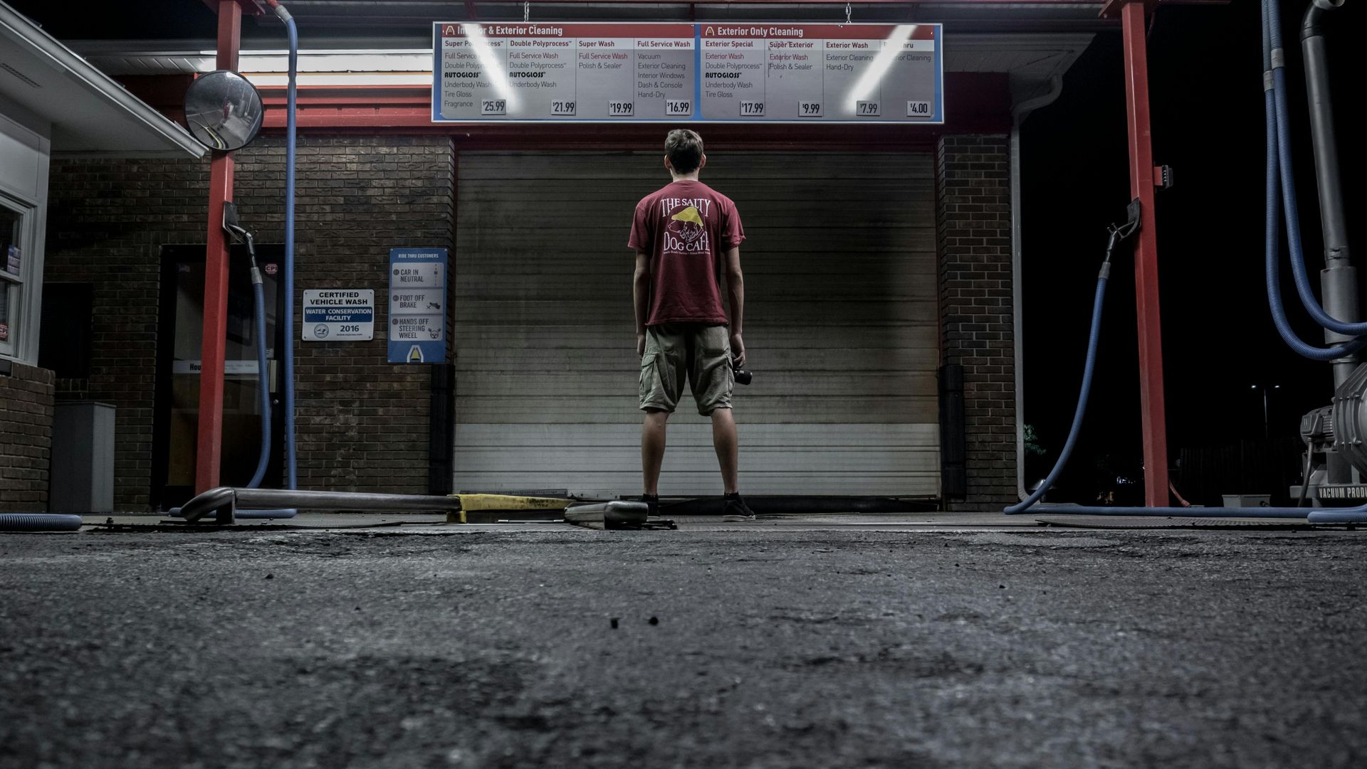 A man in a red shirt is standing in front of a garage door.