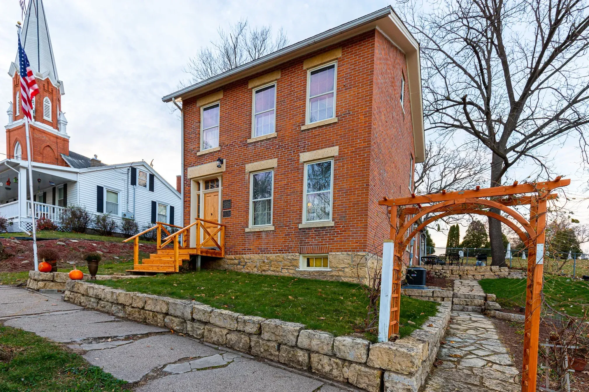 A historic red brick house with white trim stands beside a white church building under a clear sky.