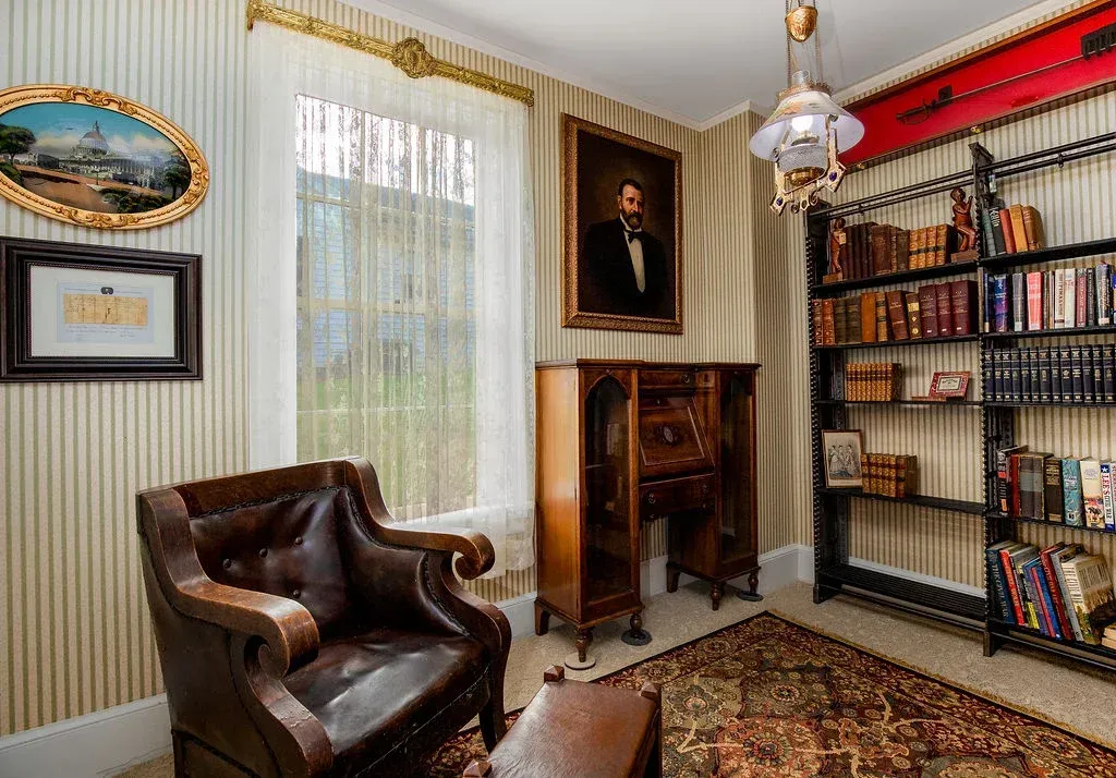 A traditional study featuring a leather armchair, a wooden secretary desk, and floor-to-ceiling shelves filled with books.