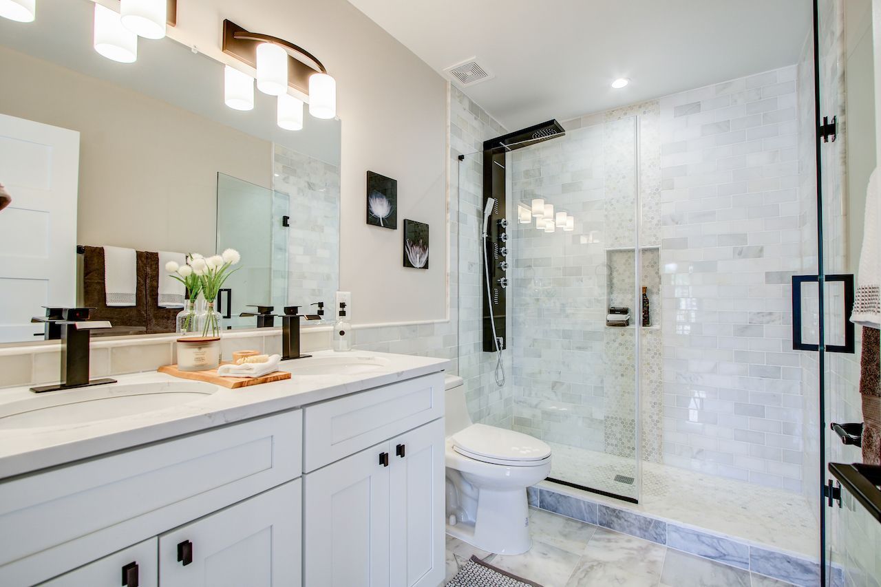 White bathroom with marble tiles, glass shower, white vanity, and black fixtures.