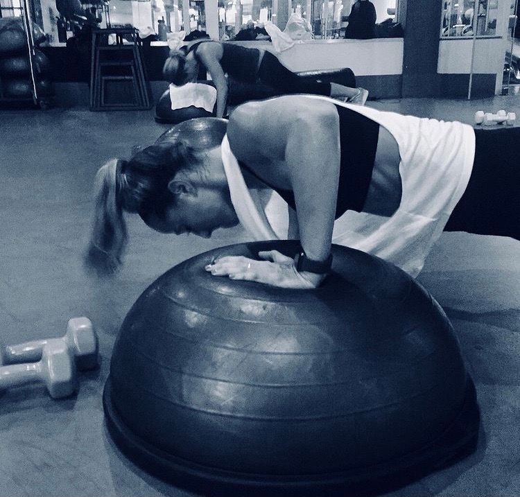 A woman is doing push ups on a half ball in a gym