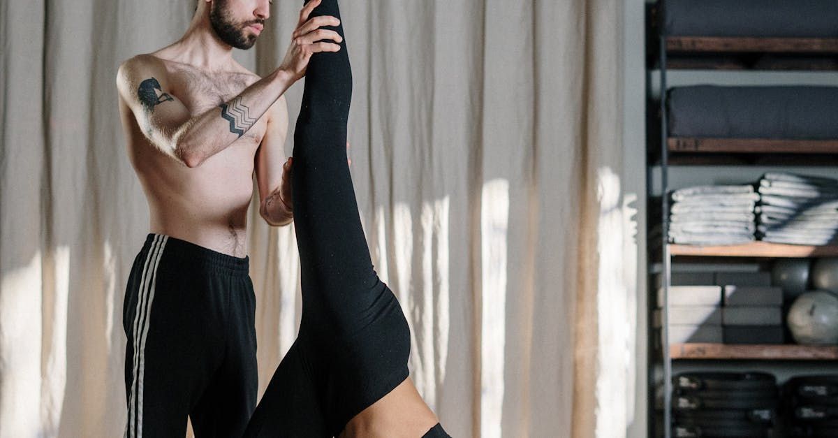 A man is helping a woman do a yoga pose in a gym.