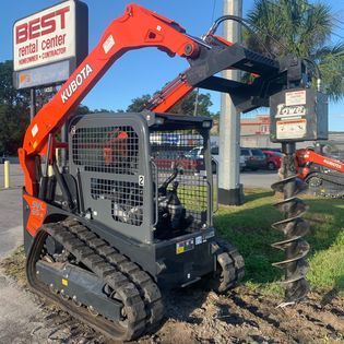 A tractor with a drill attached to it is parked in front of a best rental center sign.