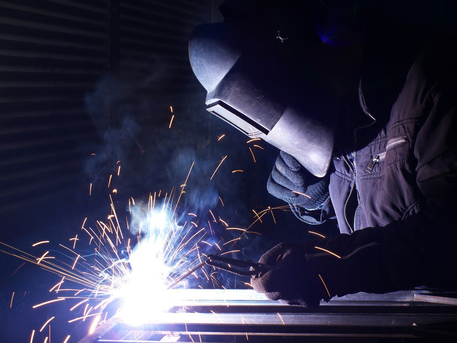 A man wearing a welding mask is welding a piece of metal