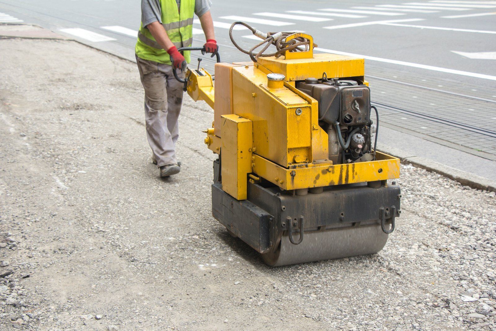 A man is pushing a yellow roller on a road.