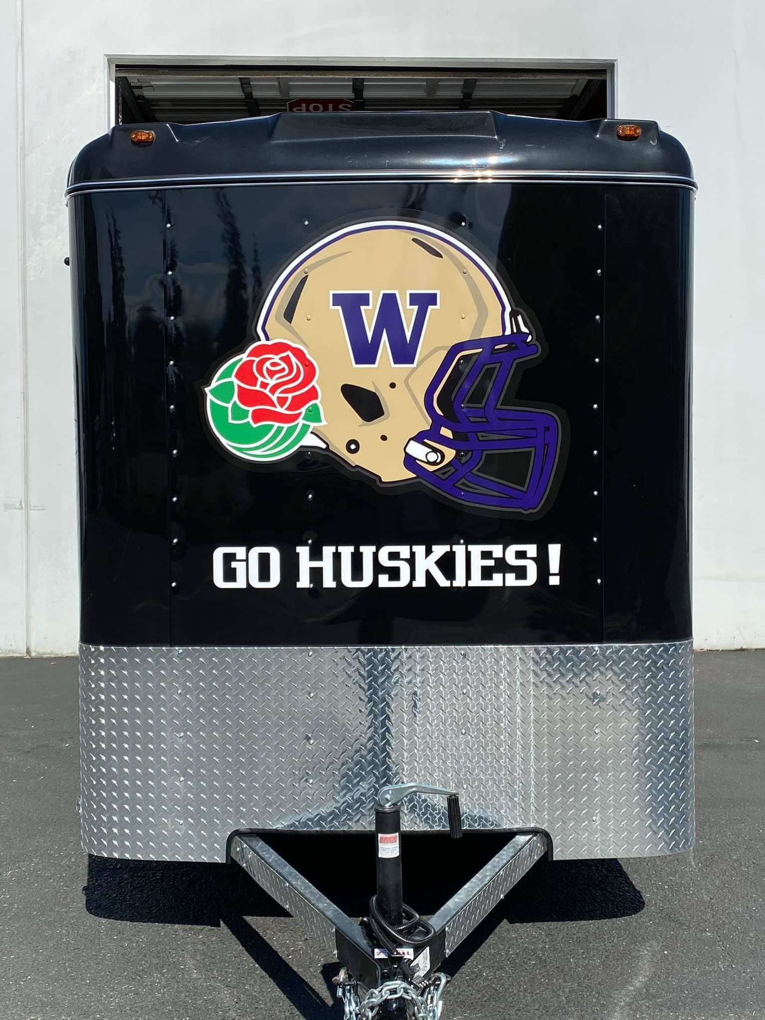 A black cargo trailer features a gold Washington Huskies football helmet with a rose logo and