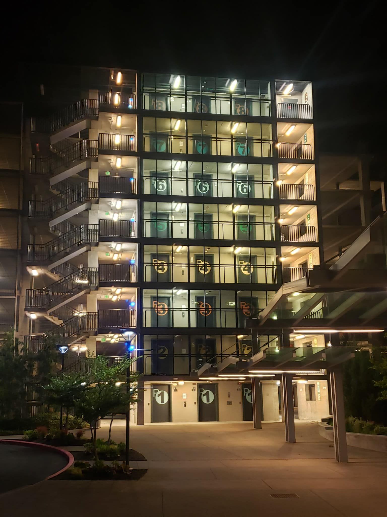 A brightly lit, multi-story modern parking structure at night with numbered levels and an exterior staircase.