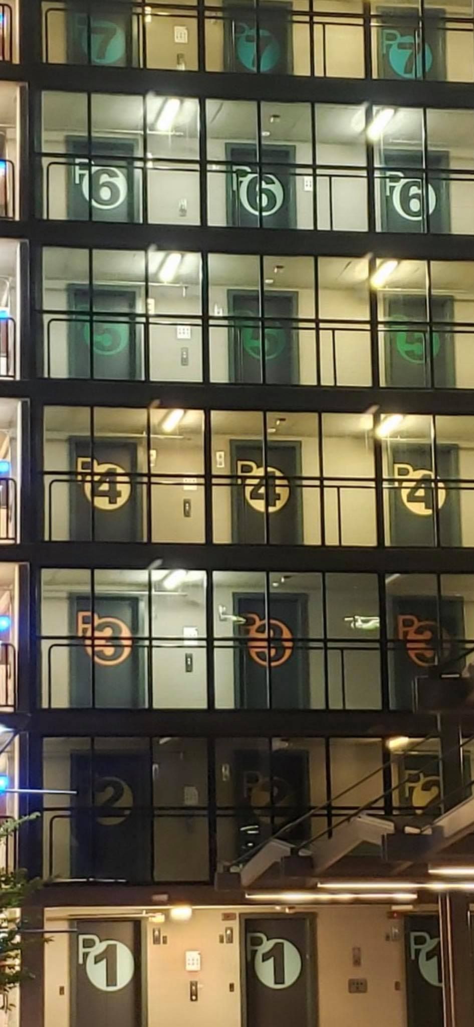 A glass-walled parking garage with numbered floor levels displayed on the doors, from P1 at the bottom to 7 at the top.
