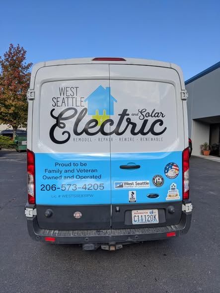 Rear view of a West Seattle Electric & Solar work van, white and light blue, with company name, phone number, and logo.