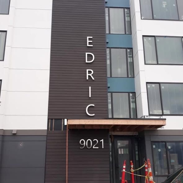The building entrance at 9021 Edric, featuring dark brown siding, vertical signage, and a modern exterior design.