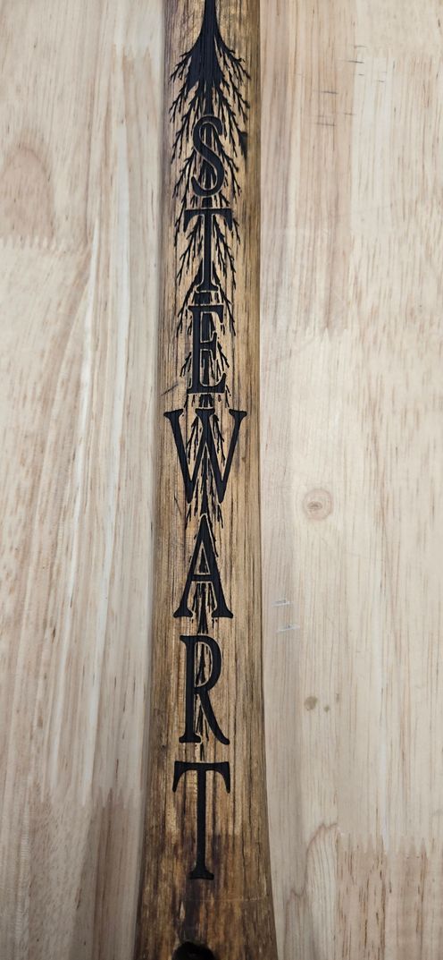Vertical wooden paddle with carved black lettering hanging against a light wood wall.
