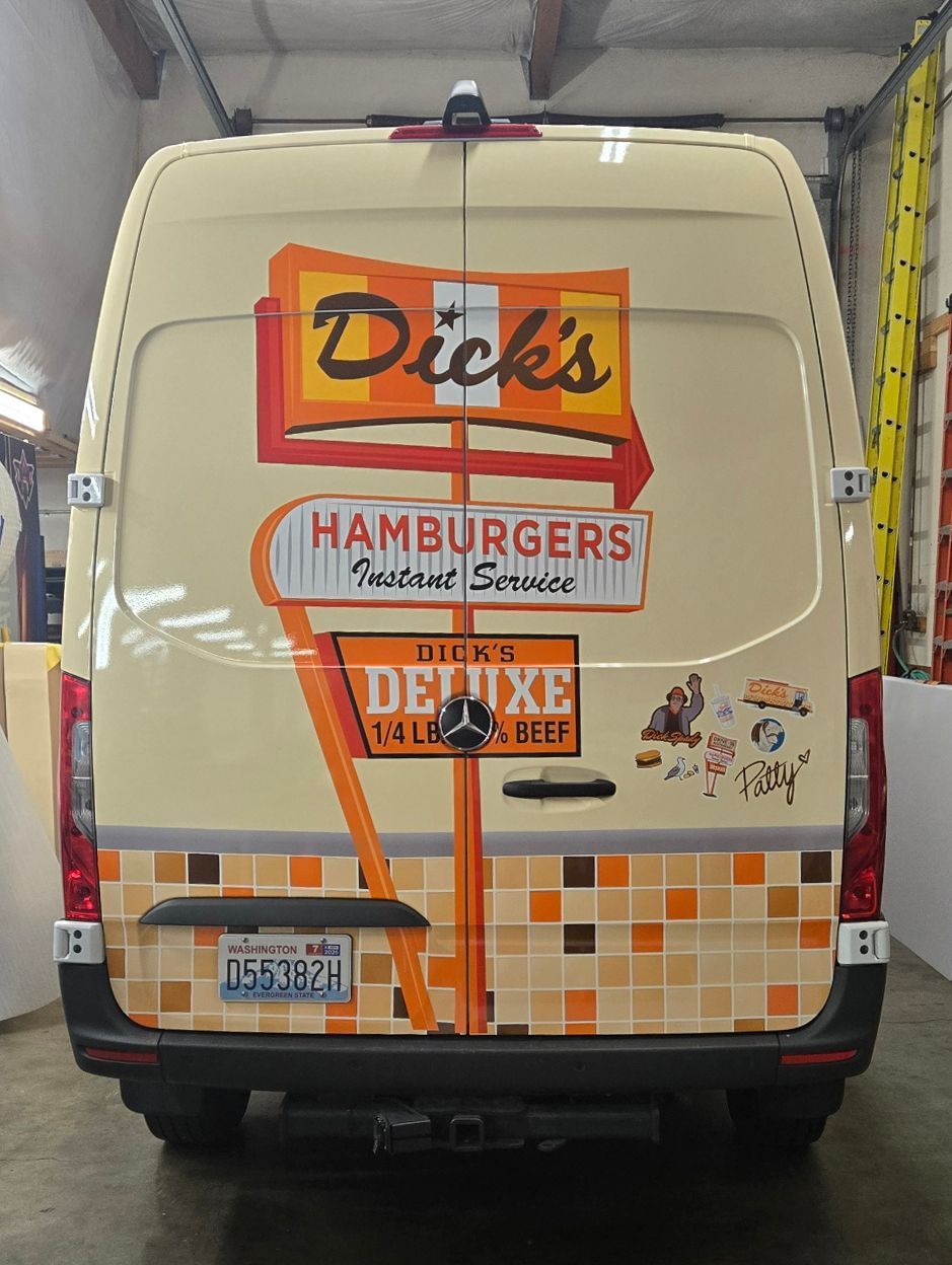 Cream-colored van rear with colorful Dick's Hamburgers and Deluxe decals strapped with orange tape.