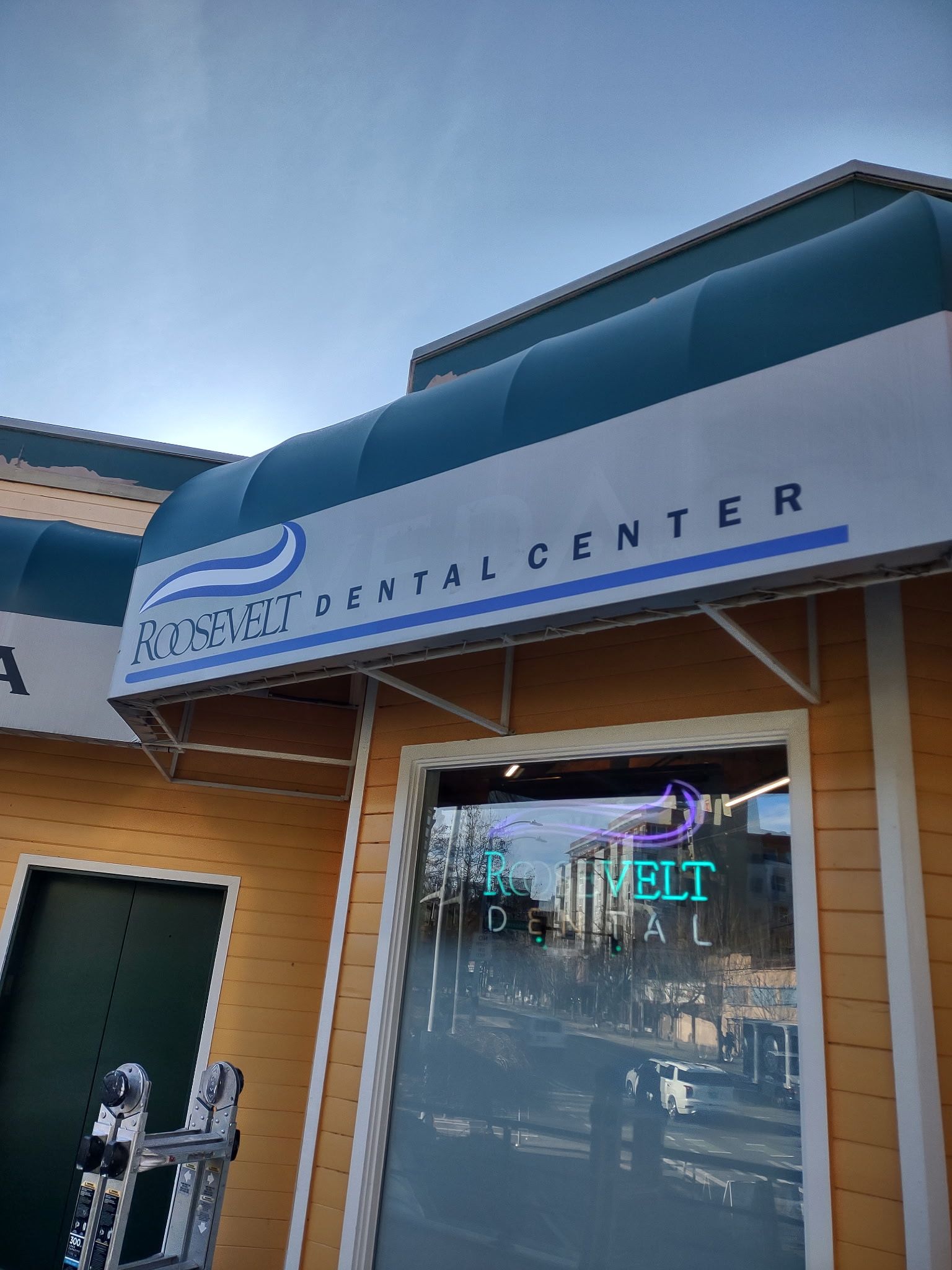 Dental center storefront with blue awning and a glass entrance door at dusk