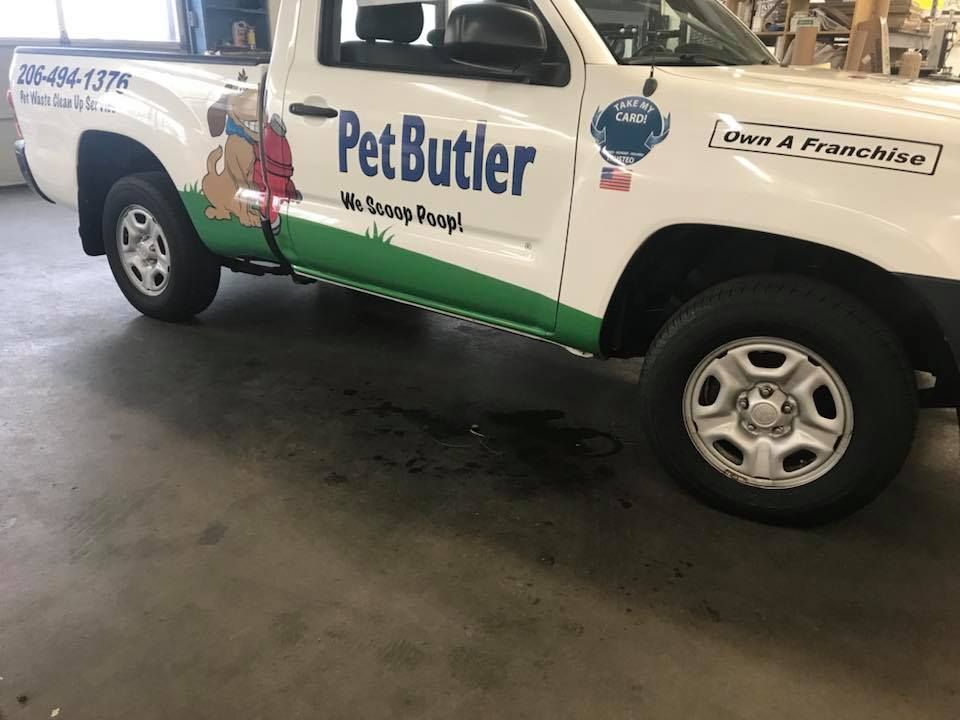 A white Pet Butler pickup truck with green graphics parked on a concrete floor with a dark fluid leak underneath.