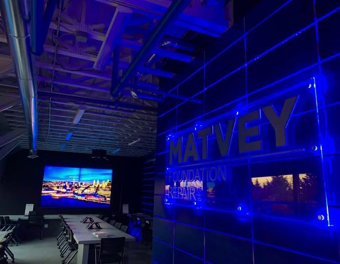 Blue-lit modern office lounge with TVs, tables, and large MATVEY wall lettering