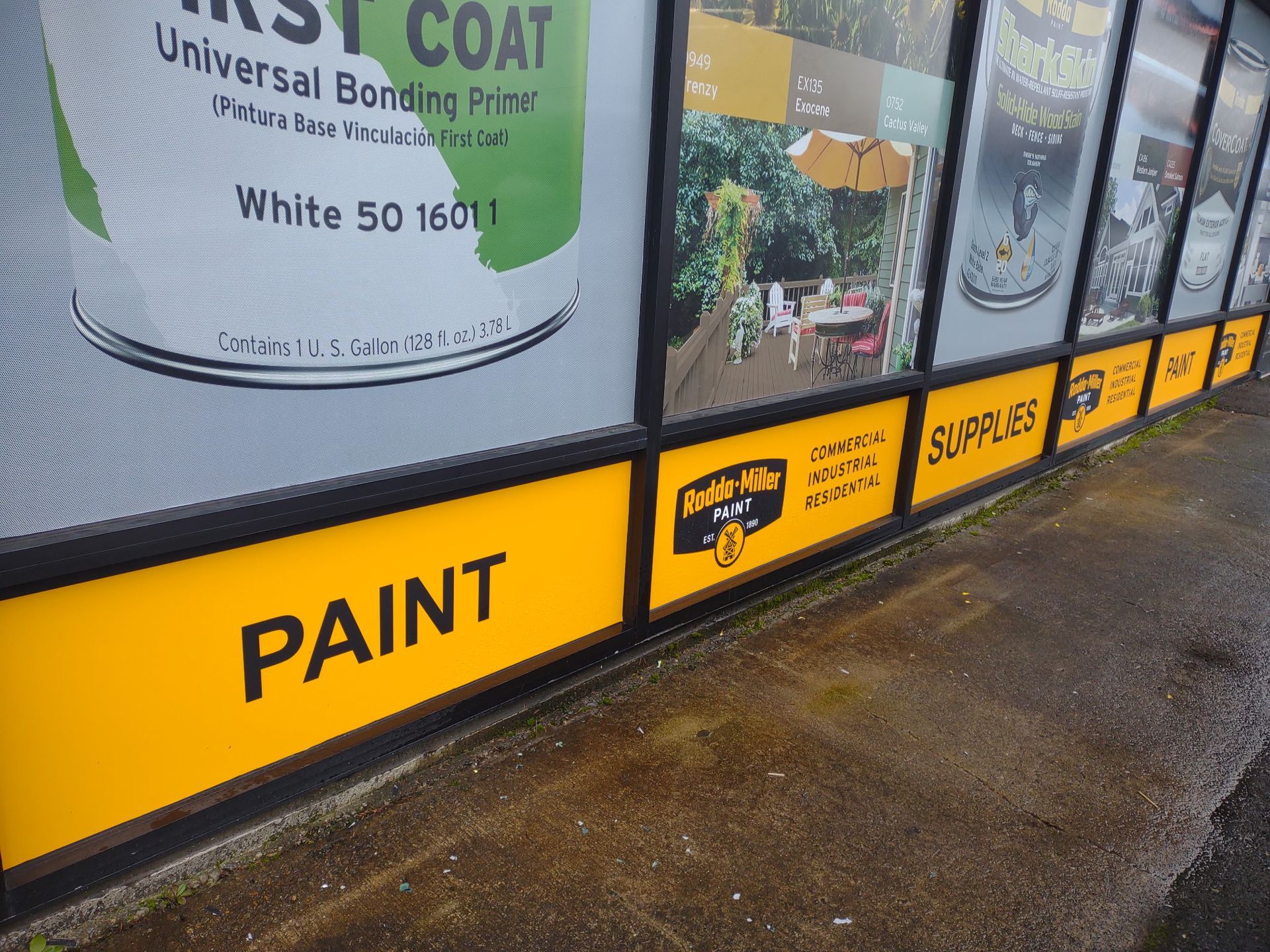 Storefront windows feature advertisements for paint and supplies, with yellow base panels displaying the text