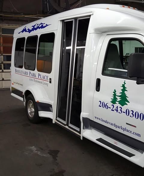 A white shuttle bus parked indoors with blue branding, a tree logo, and contact information on its side.