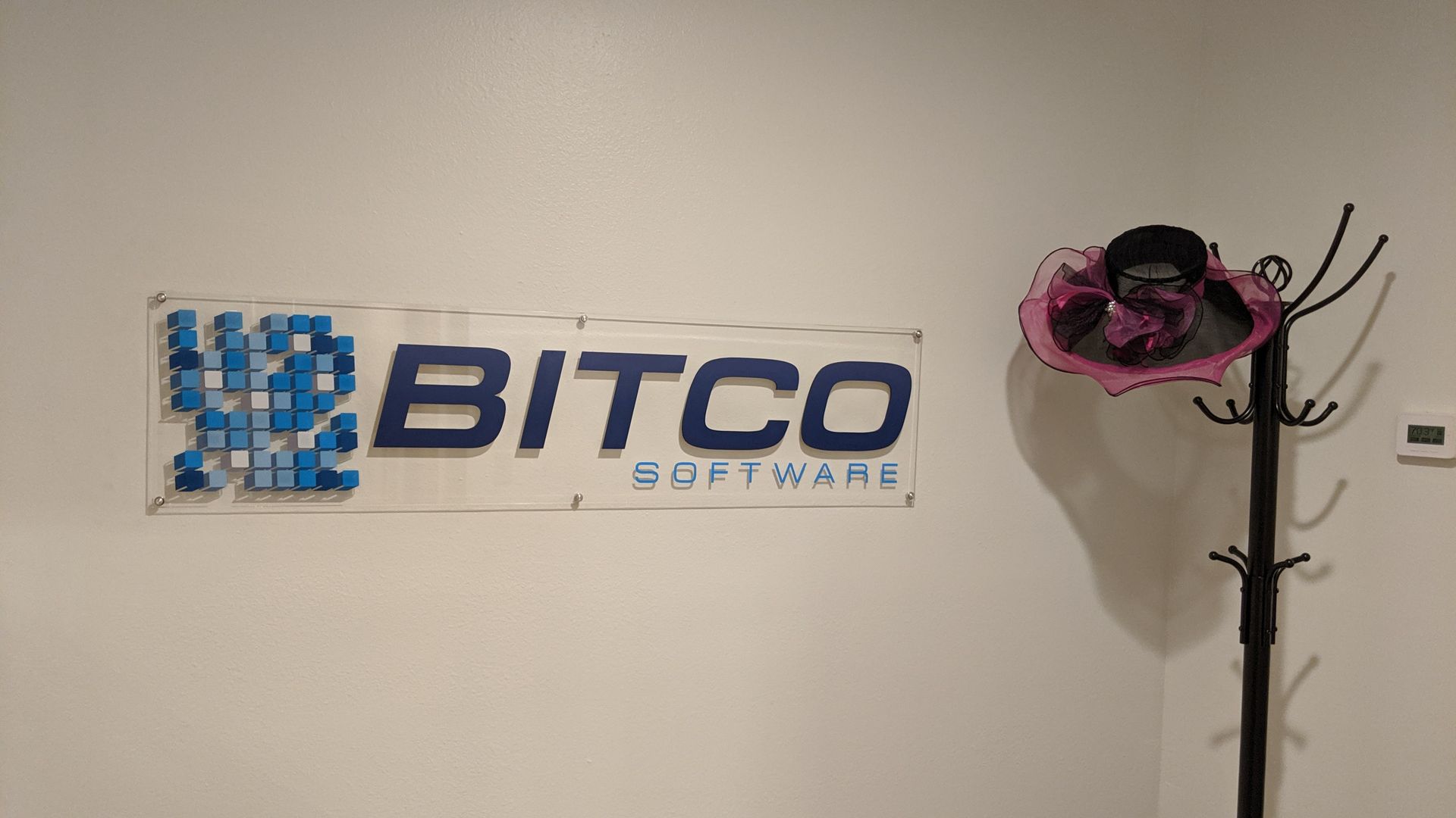The Bitco Software logo in blue on a white wall, with a decorative hat on a coat rack nearby.