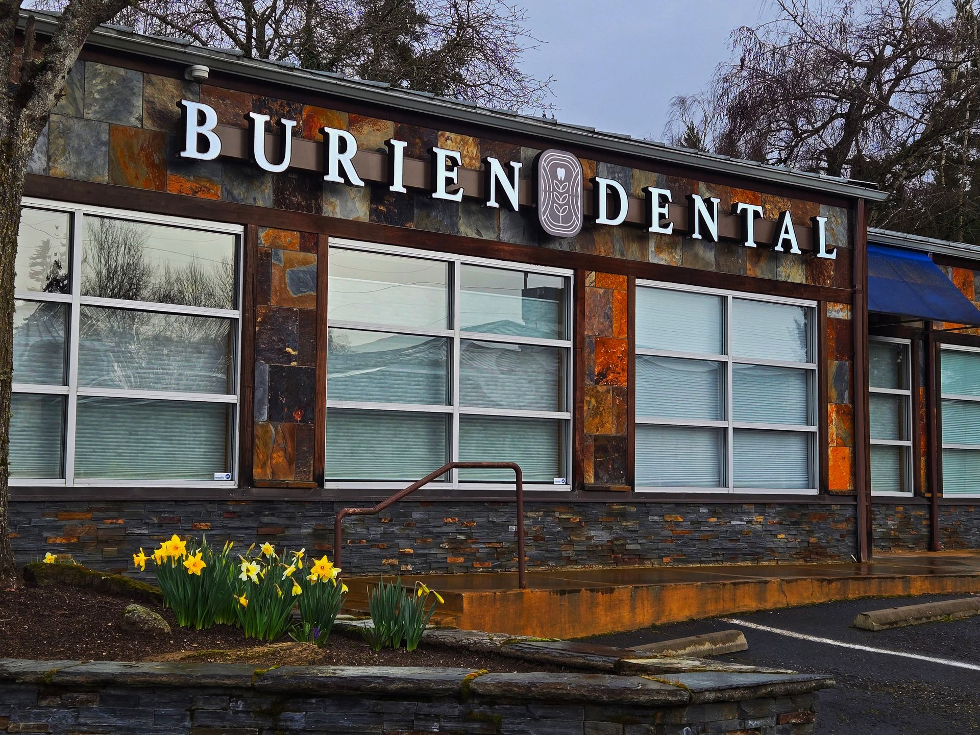 Exterior of Burien Dental with stone facade and large windows under a cloudy sky.