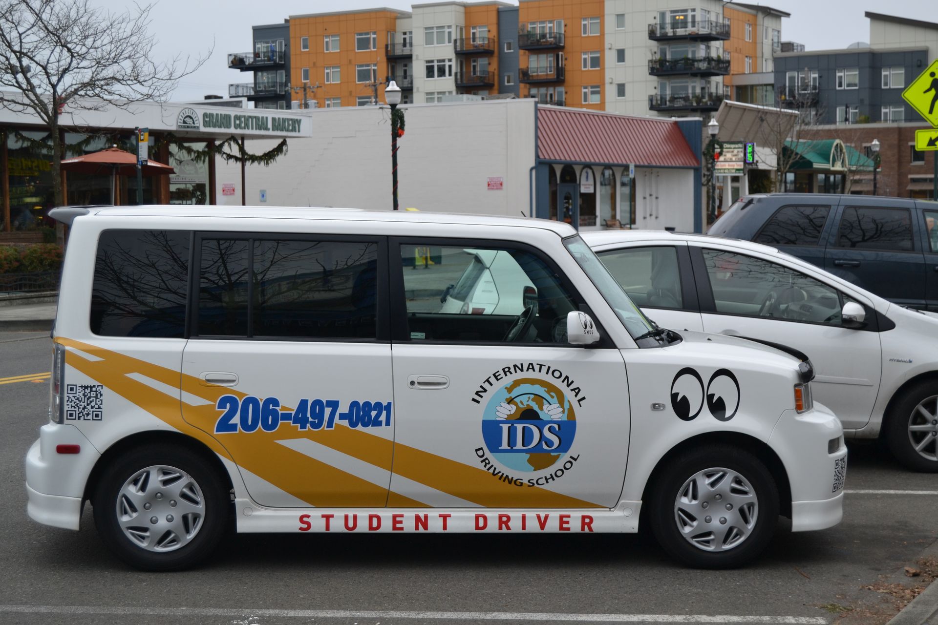 A white student driver car with a yellow graphic, 