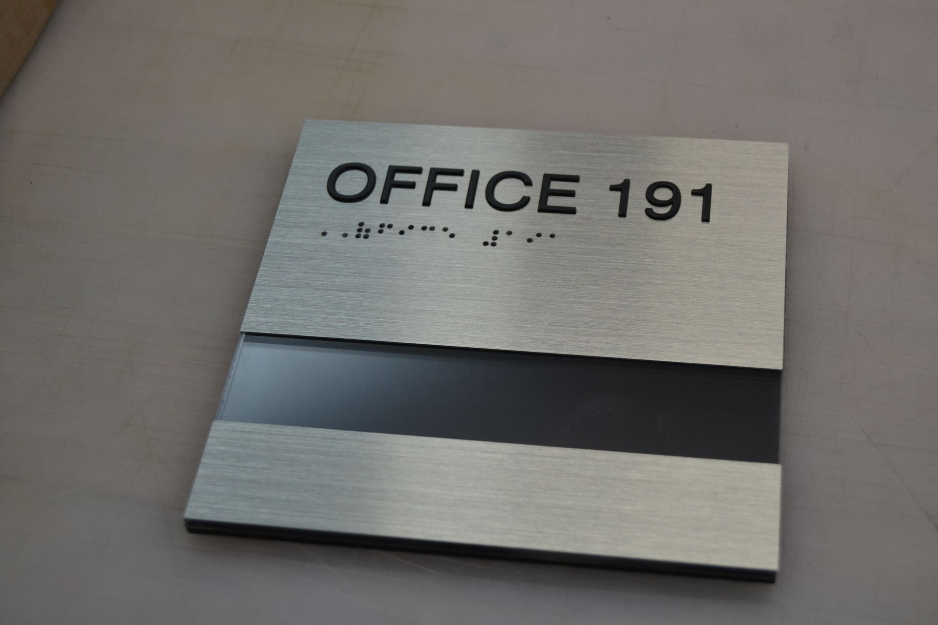 A brushed metal office door sign labeled 