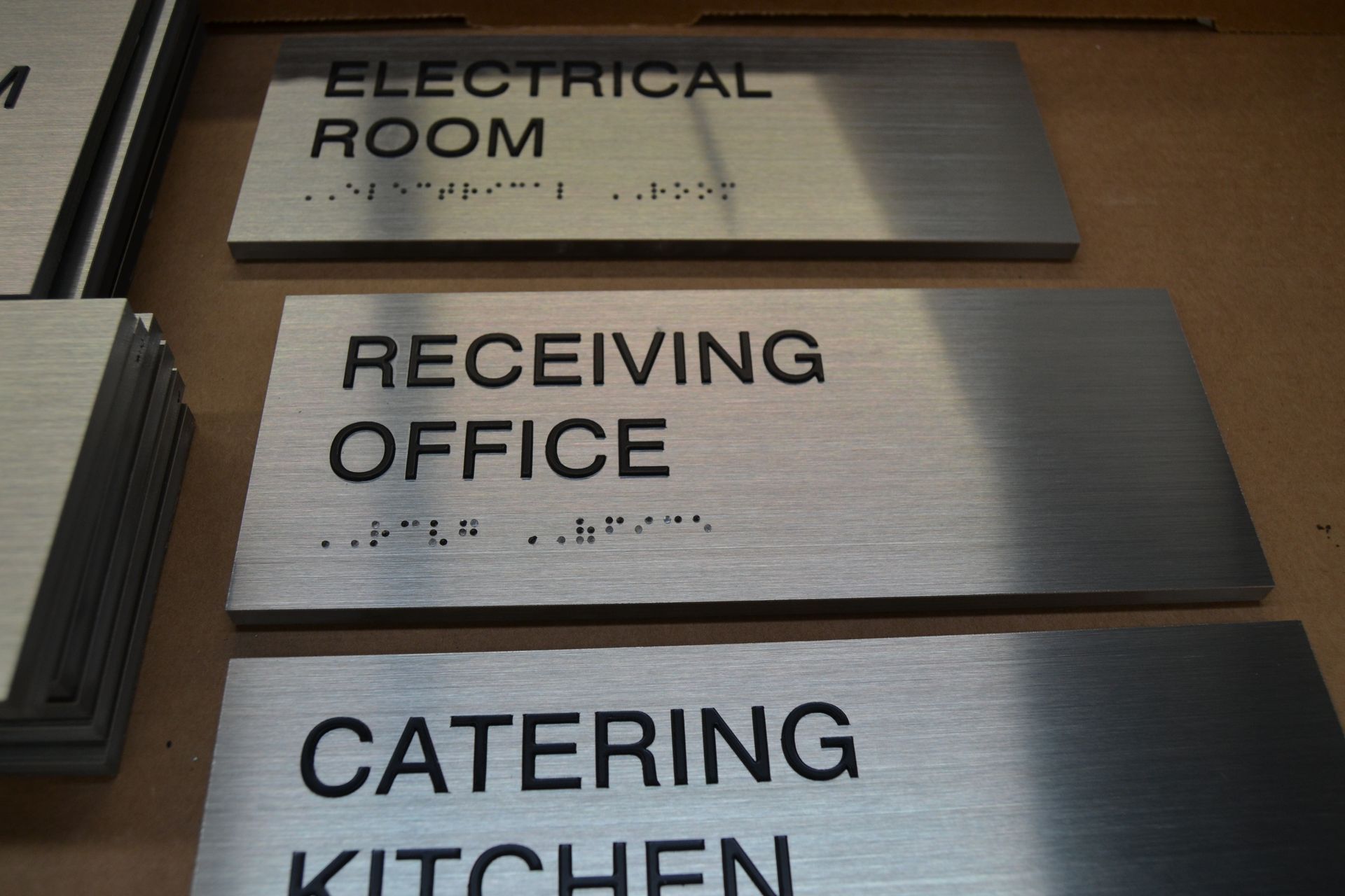 Several brushed-metal signs with black lettering and braille, reading 