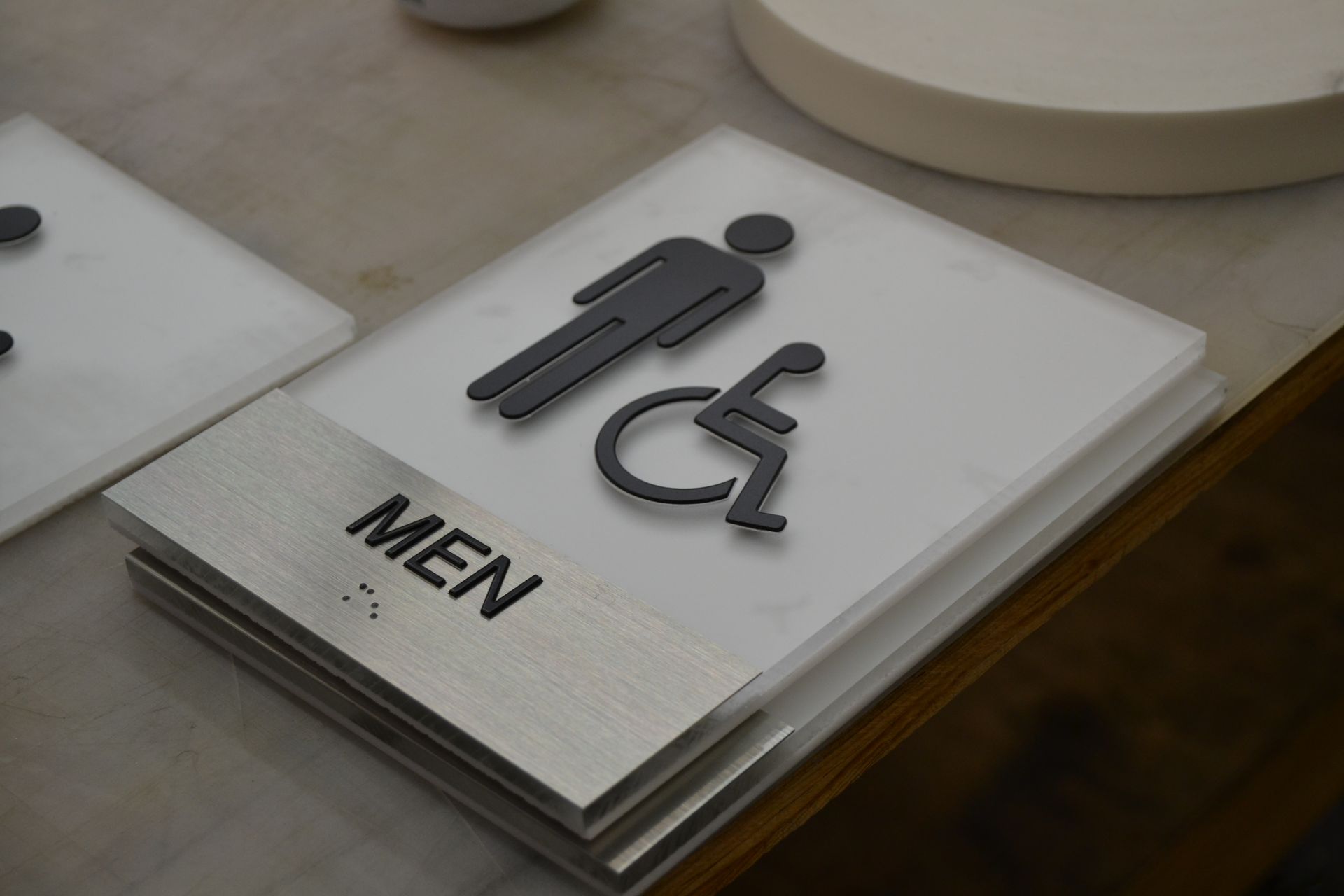 A sign for an accessible men's restroom featuring a black wheelchair icon and the text 