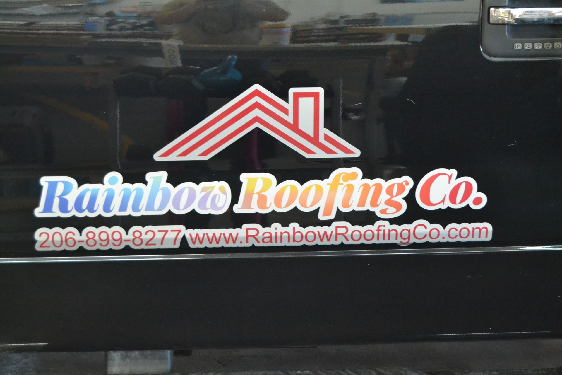 A decal for Rainbow Roofing Co. on a black vehicle, featuring a red roof icon, brand name, phone number, and website.