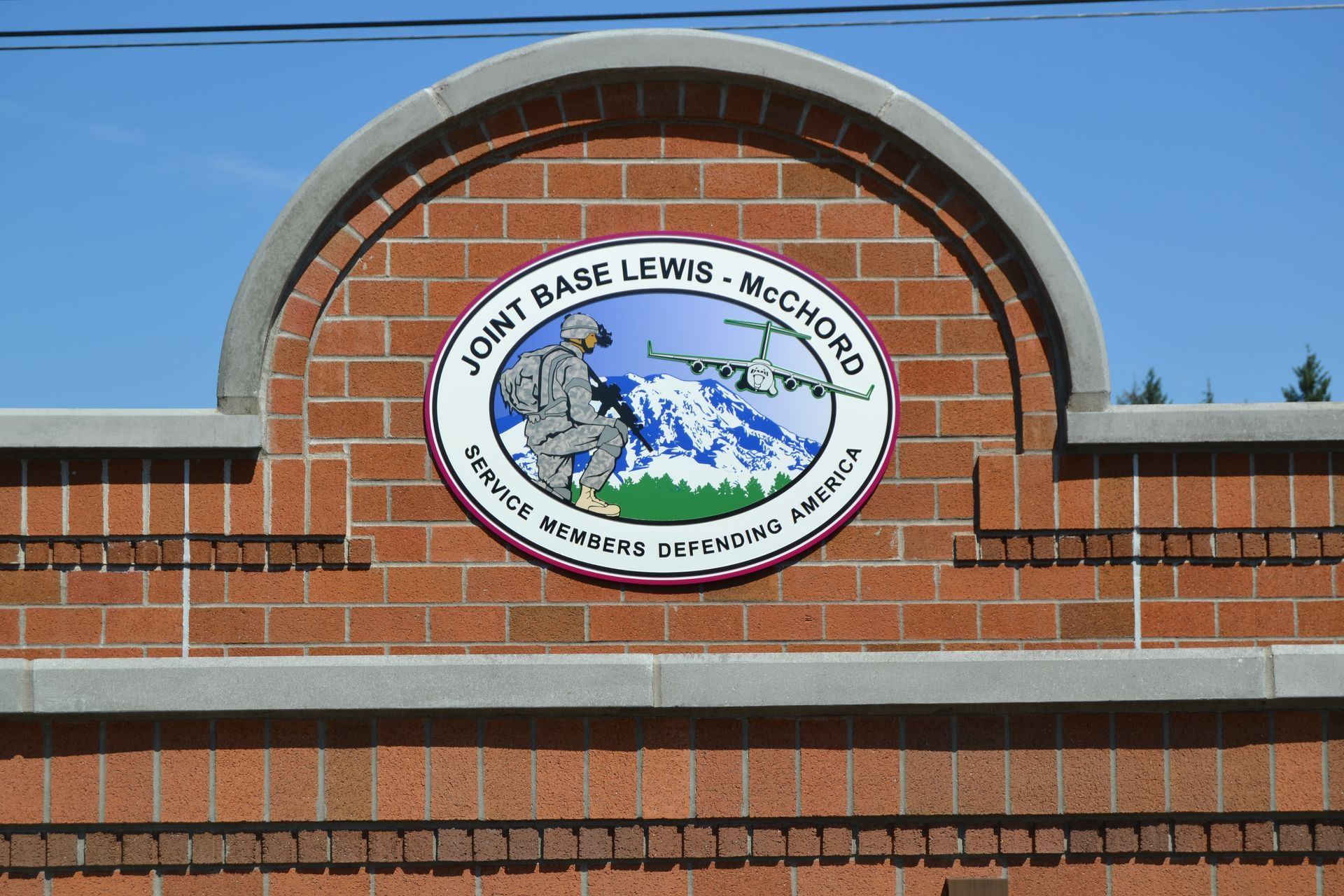 A brick archway displays the circular logo for Joint Base Lewis-McChord, featuring a soldier, aircraft, and mountain.