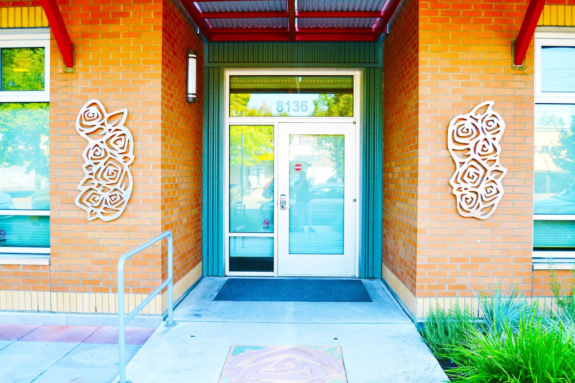 The building entrance has a glass door between orange brick walls, each decorated with a white floral metal sculpture.