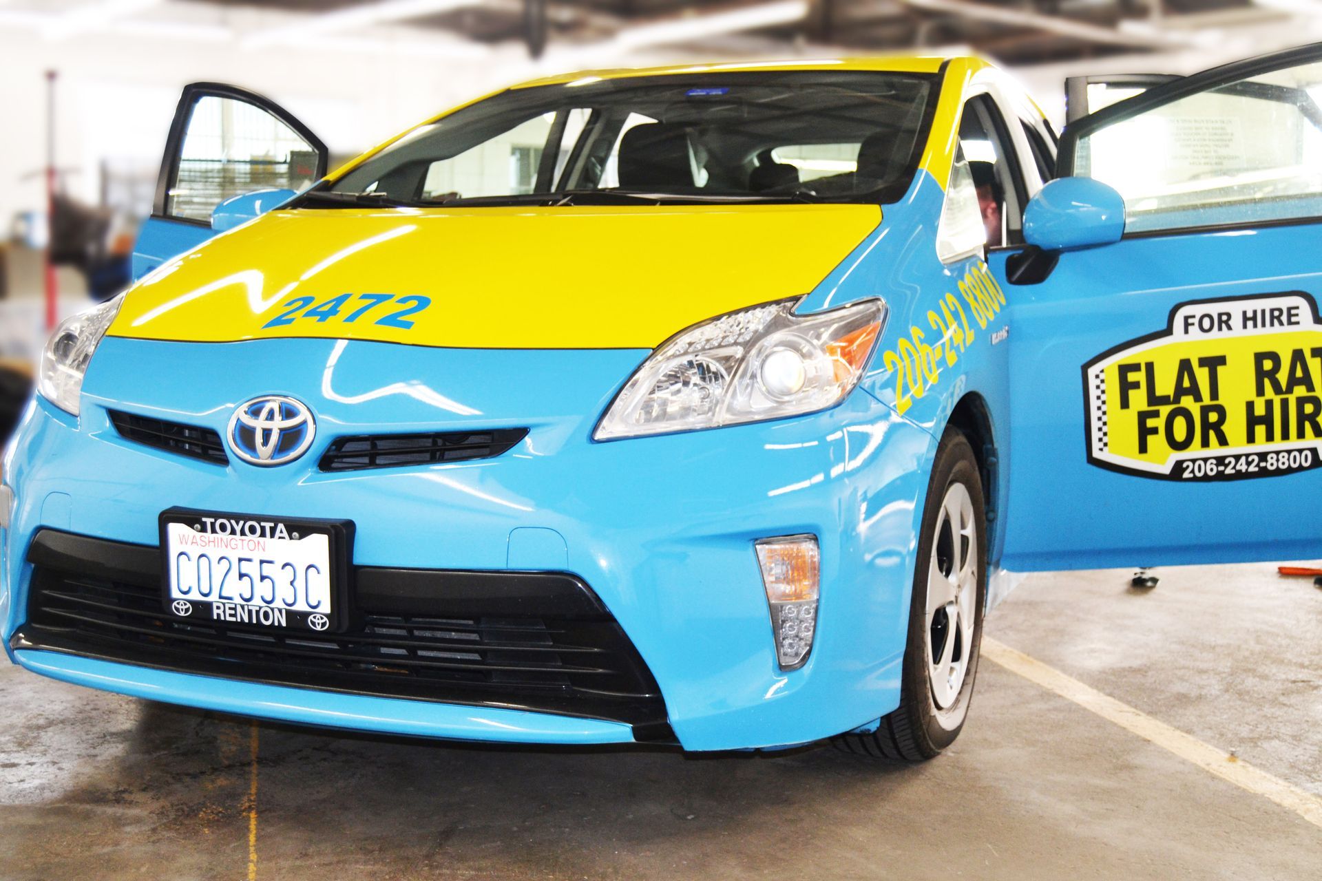 A bright blue and yellow taxi cab parked in a garage with its driver-side door open.
