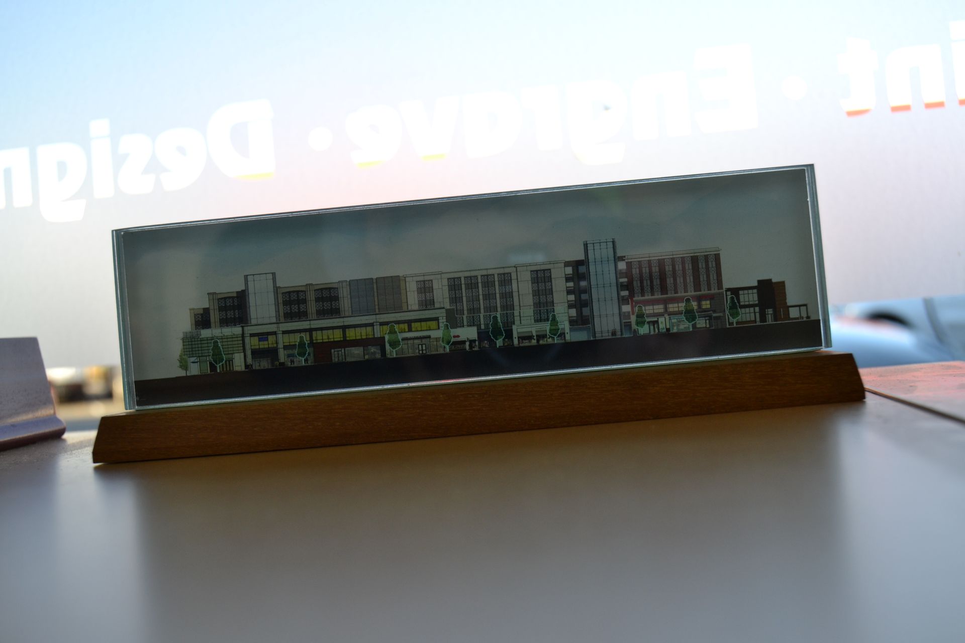 A rectangular glass desktop award features a miniature architectural print of a modern multi-story building on a wood base.