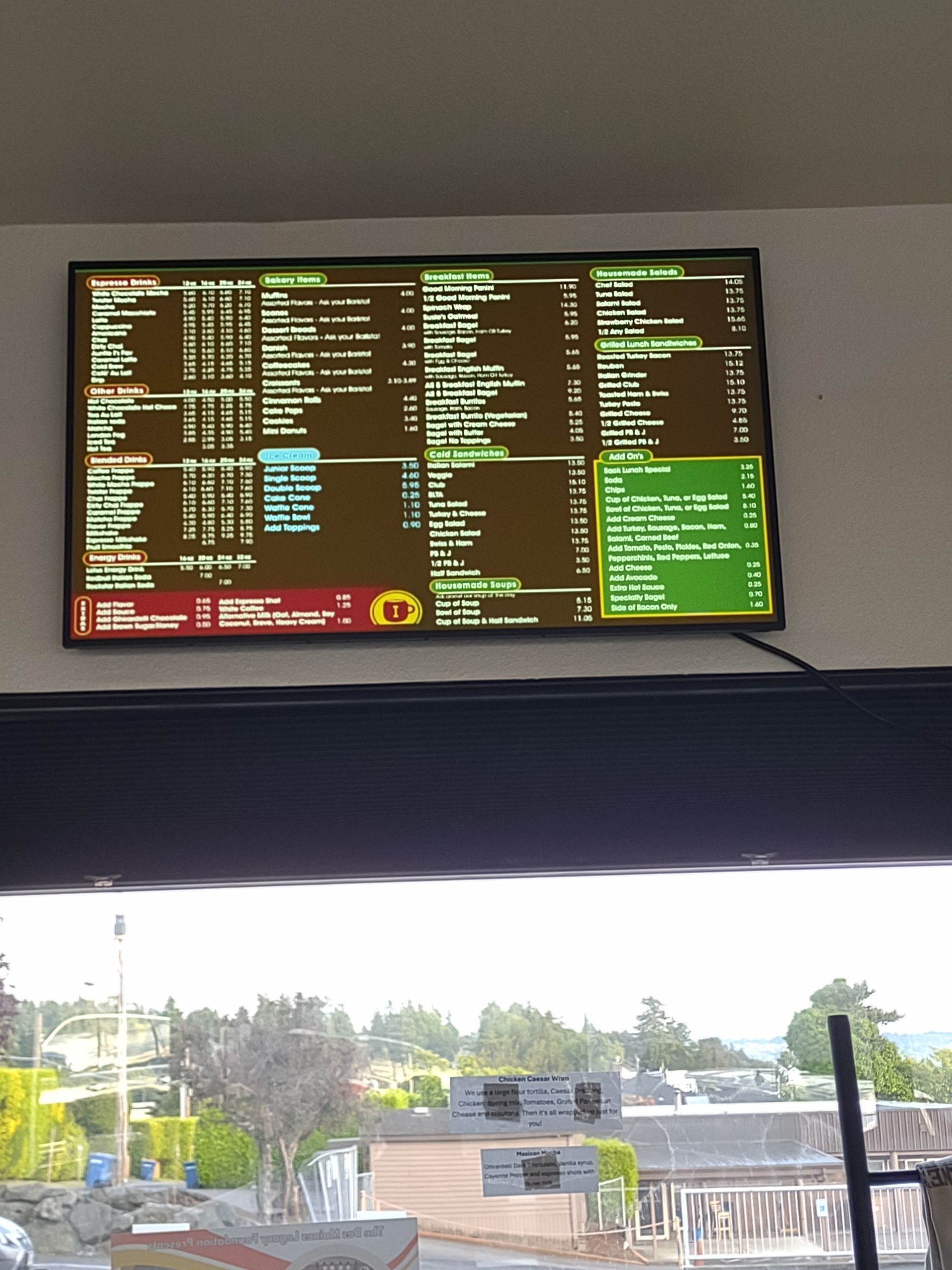 Digital menu board hanging on a wall showing various food items, prices, and categories in a restaurant setting.