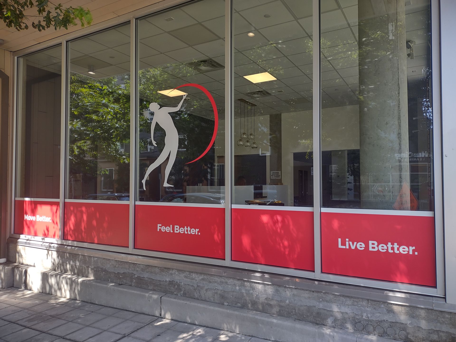 Storefront window with a white logo of a person stretching, and red panels below with the text