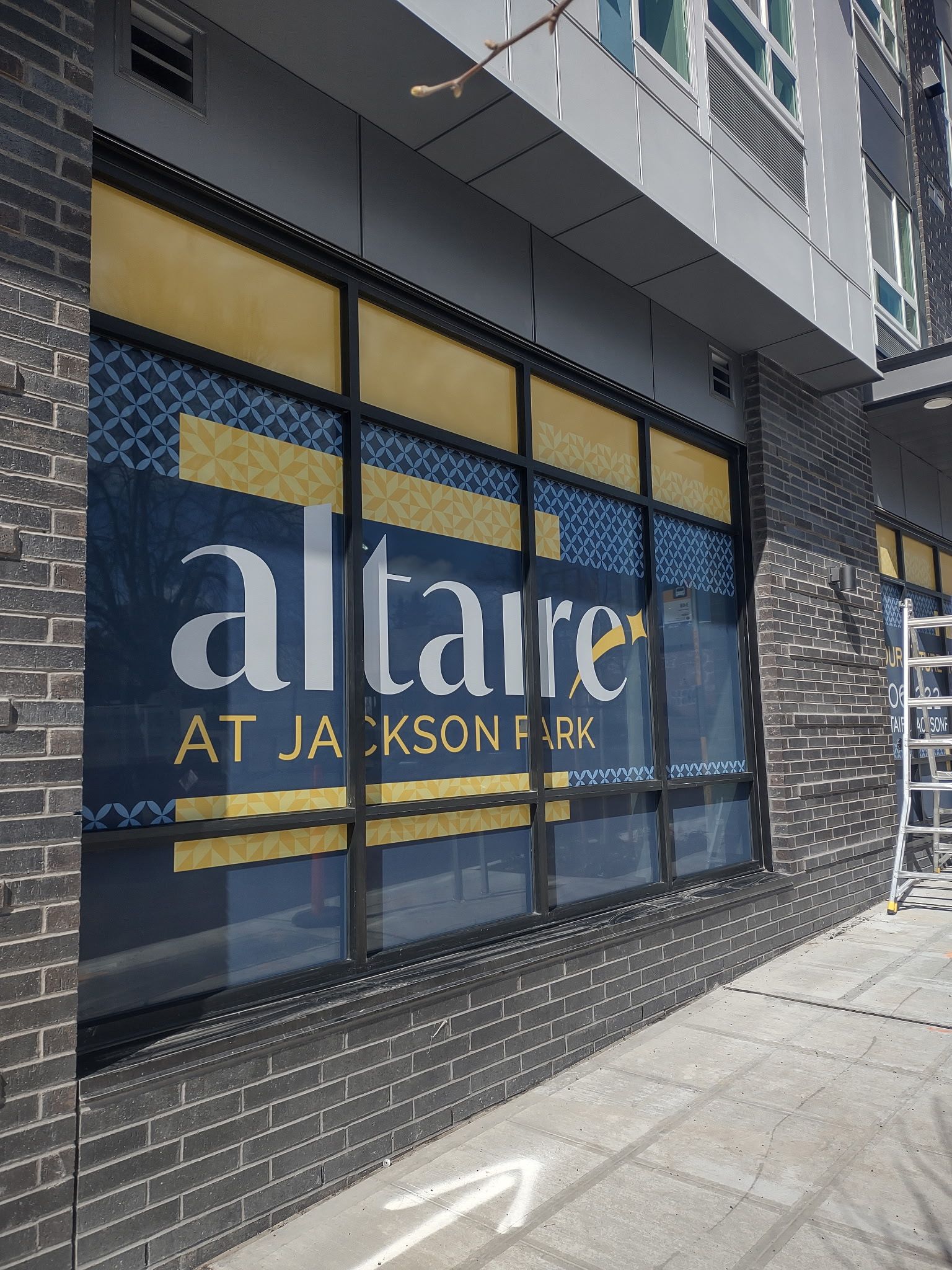 Storefront window sign for “altair at Jackson Park” on a brick building.