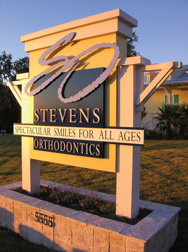 A yellow and black monument sign for Stevens Orthodontics, featuring their logo and the text.