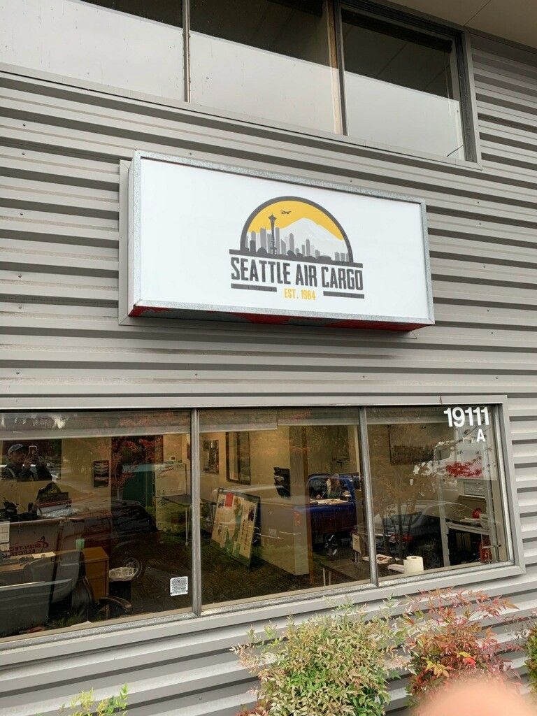 The storefront sign for Seattle Air Cargo features a yellow sun logo with a mountain and city skyline silhouette.