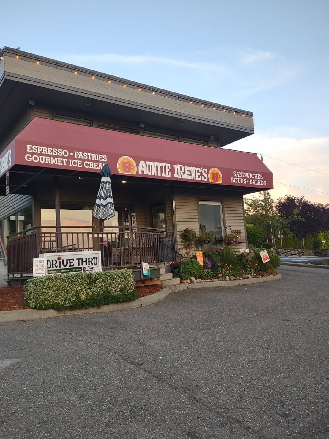 A Little Irene’s storefront with a red awning, outdoor seating, and a drive-thru sign at dusk.