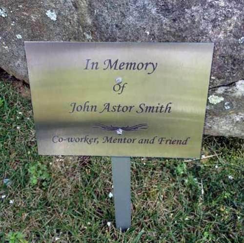 A metal memorial plaque on a stake in the grass, engraved with 