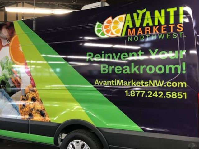A dark purple van with the Avanti Markets Northwest logo, phone number, and website, featuring citrus fruit graphics.
