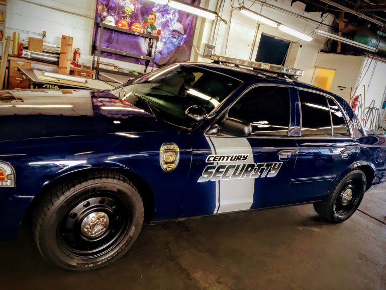 A dark blue Century Security sedan parked inside a garage, featuring a white side stripe and a badge decal.
