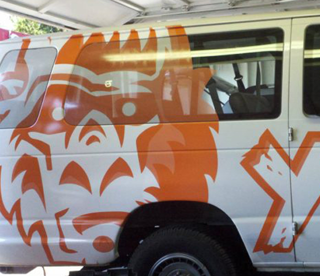 A side view of a white van featuring a large orange graphic of a stylized monkey face on the rear panel.