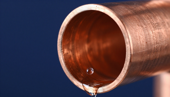 Close-up of a copper pipe with a small droplet of water at the opening against a blue background